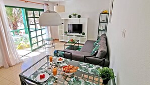 A modern living room with a TV, sofa, and dining area with breakfast. - Apartment PALM GARDEN - Costa Calma - Fiber Optic Internet - Pool (Costa Calma)