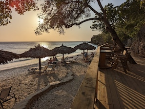 Une terrasse en bois avec des chaises longues et des parasols en chaume, sur une plage.