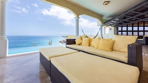 A sunlit outdoor seating area with a view of the ocean, featuring wicker furniture and a hammock. - Award-Winning Luxury Beach-Side Villa - Wrap-around Infinity Pool -Pickleball (Sabana Westpunt)