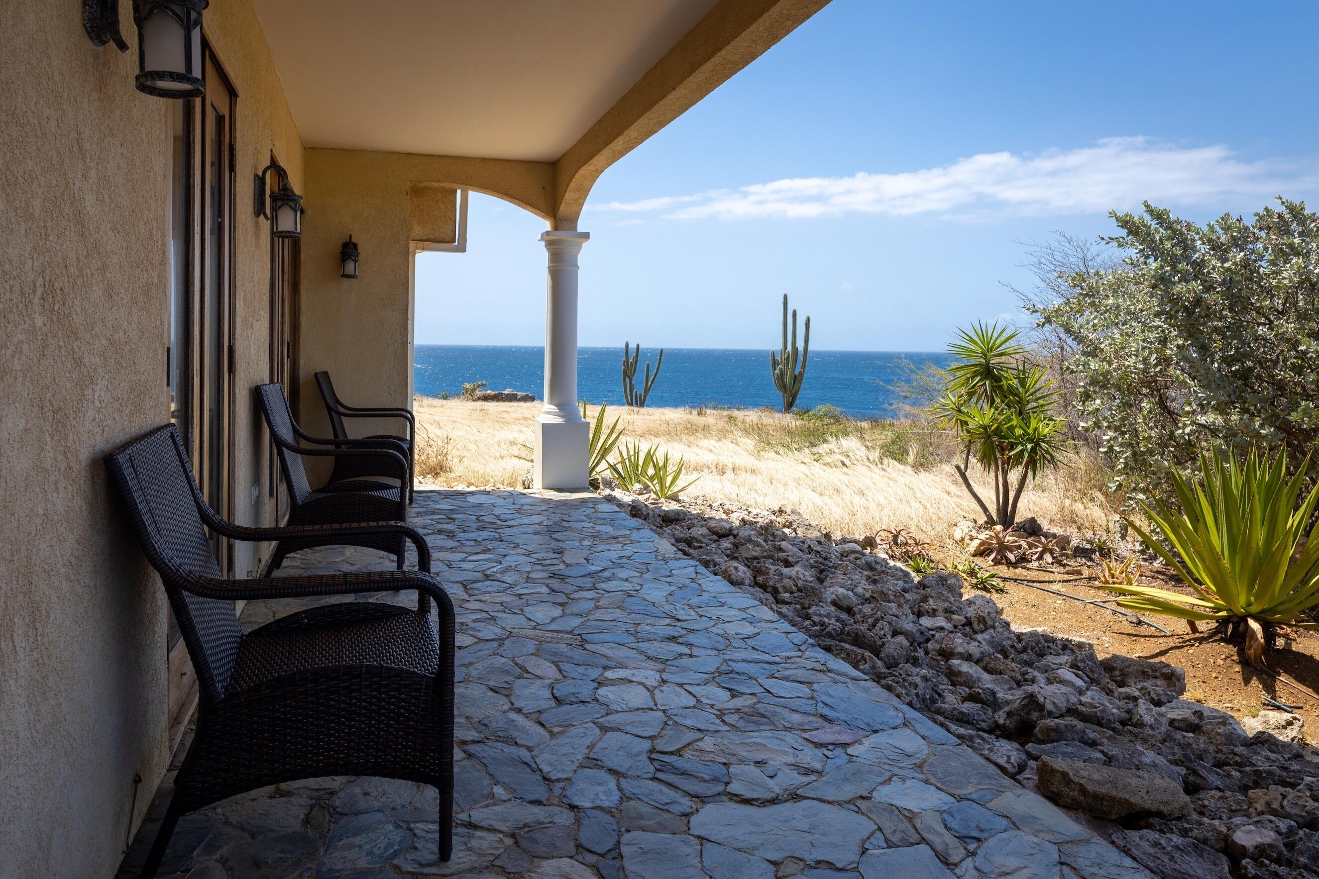 Eine terrasse mit Steinplatten, zwei Korbstühlen, einem Kakteengarten und Blick auf das Meer.