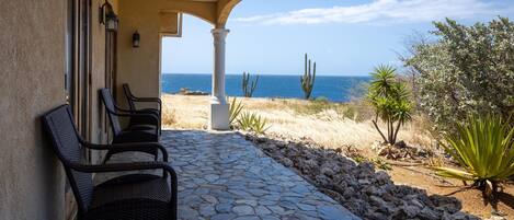 Eine terrasse mit Steinplatten, zwei Korbstühlen, einem Kakteengarten und Blick auf das Meer.