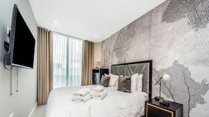 A modern hotel room with a large bed, a flat-screen TV mounted on the wall, and a decorative wall mural.