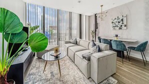 A modern living room with a sectional sofa, a round coffee table, and a dining area with a white table and blue chairs.