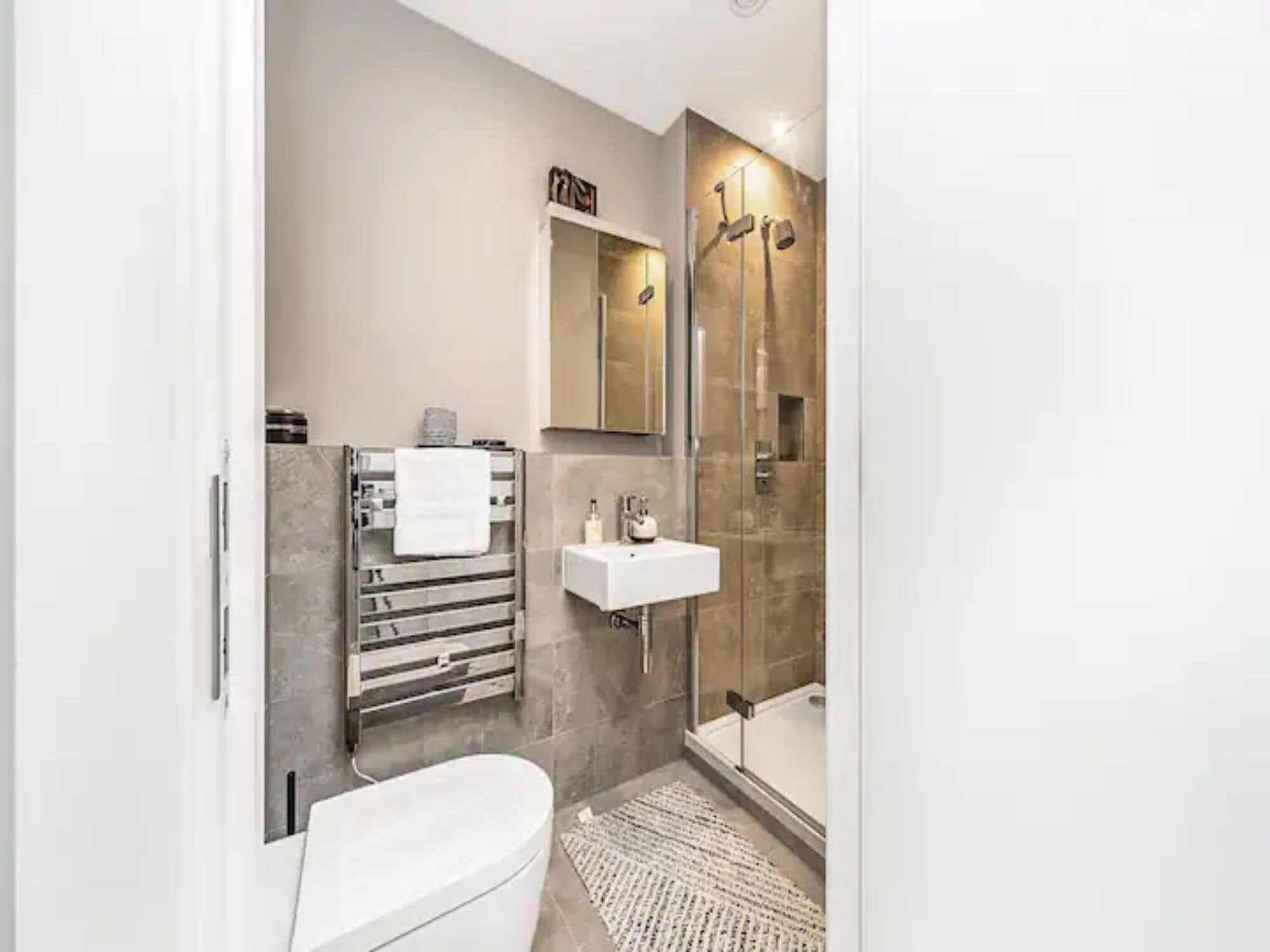 A modern bathroom with a white toilet, a glass shower enclosure, and a white sink with a mirror above it.