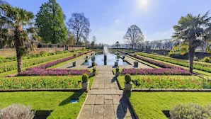 A formal garden with a central water feature, symmetrical flower beds, and palm trees.