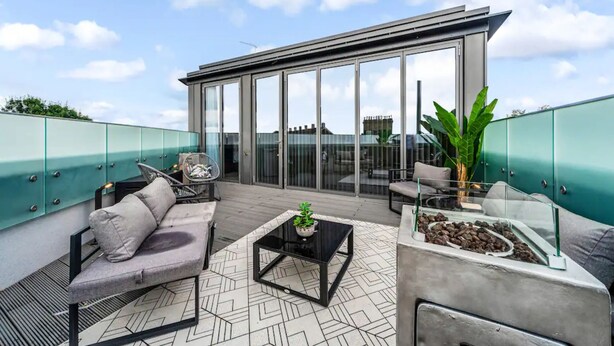 A rooftop terrace with a sofa, chairs, a coffee table, and a plant.
