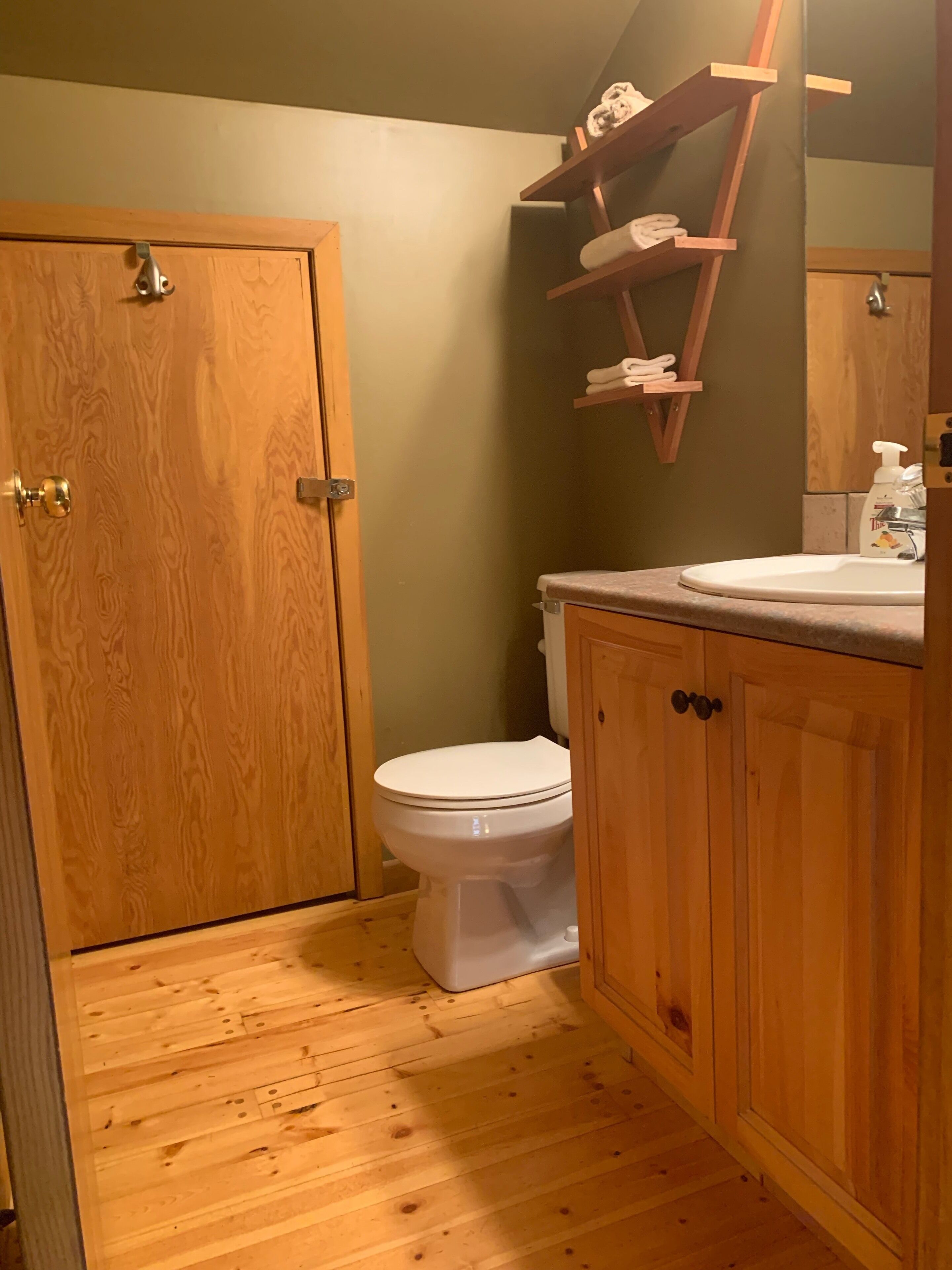 Ein Badezimmer mit Holzboden, Toilette, Holzschränken und einem Regal mit Handtüchern.
