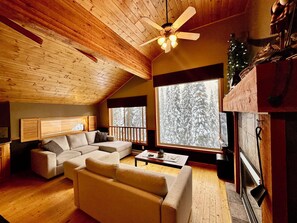 A cozy living room with a wooden ceiling, a sectional sofa, a coffee table, and a fireplace.