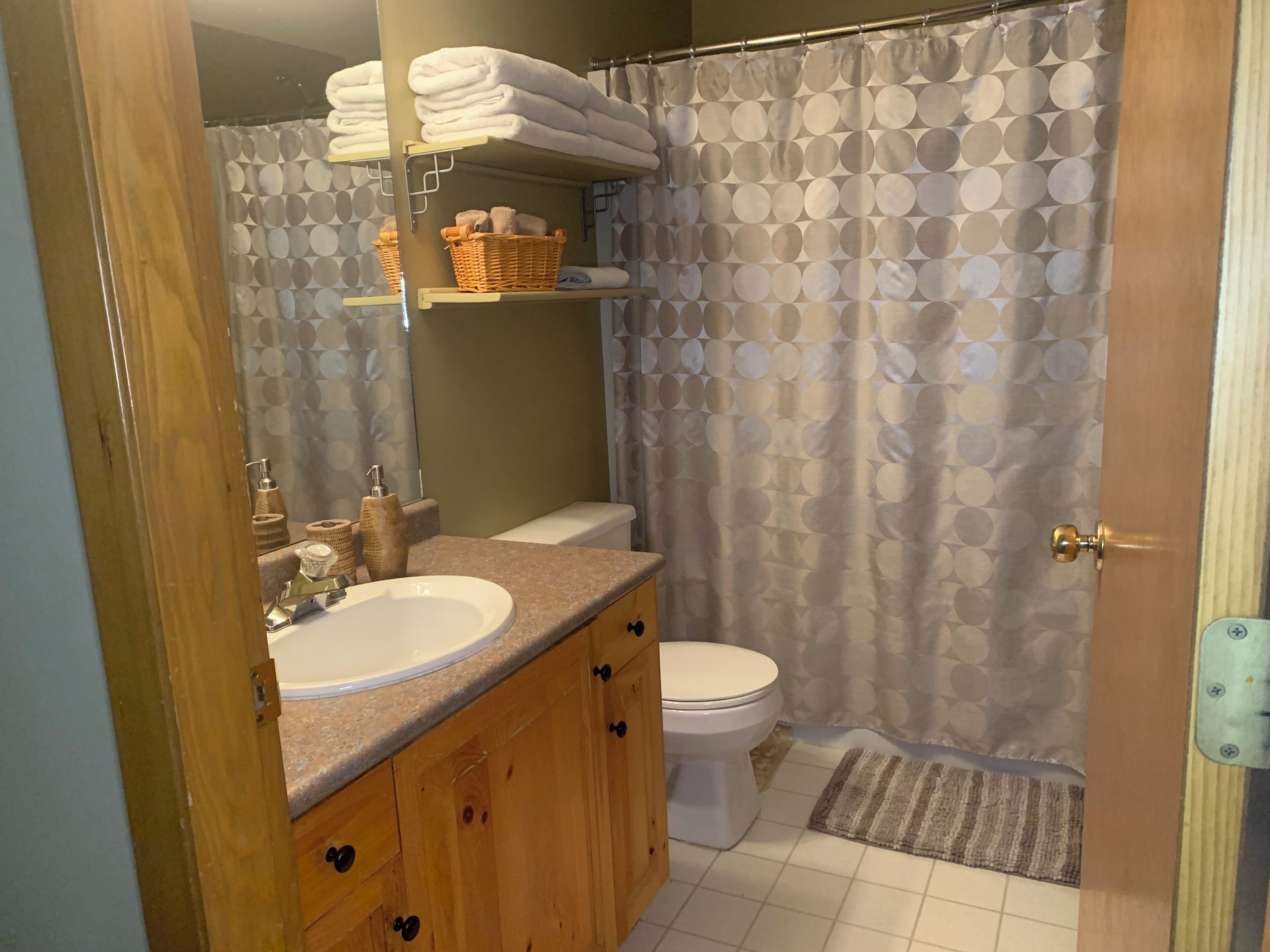 A bathroom with a wooden vanity, a white sink, a toilet, and a shower curtain with a circular pattern.
