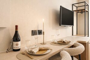 A neatly set dining table with a bottle of wine, glasses, and cutlery, a candle, and a TV mounted on the wall.