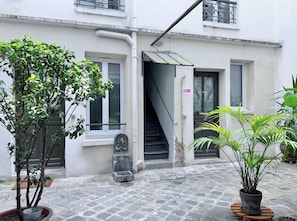 A building with a staircase leading to an entrance, a potted plant, and a metal gate.
