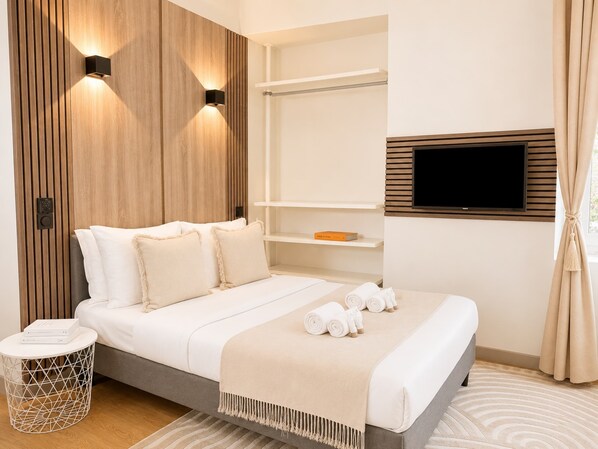 A modern hotel room with a bed, built-in shelves, a TV, and a bedside table with a lamp.