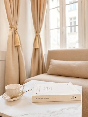 A room with a sofa, a table with a book and a cup, and curtains tied back.