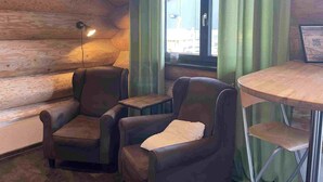 Un interior de madera con un sofá, dos sillones, una mesita y una ventana con cortinas.