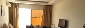 A hotel room with a large window, curtains, a flat-screen TV, and a sofa.