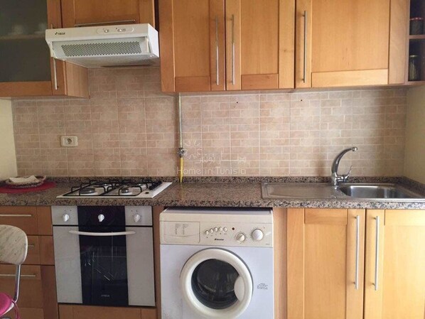 A kitchen with wooden cabinets, a gas stove, a washing machine, and a sink.