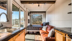 Ein kompaktes Wohnmobil-Interieur mit einer Küchenzeile, einem Bett und einem Fenster mit Blick ins Freie.