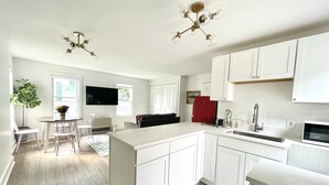 Een moderne keuken met witte kasten, een centraal eiland, een rode koelkast en een eethoek met een tafel en stoelen.