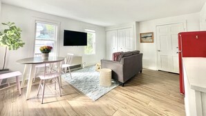 Een moderne woonkamer met een bank, een eettafel met stoelen, een aan de muur bevestigde televisie en een rode kast.