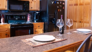 Una cocina con armarios de madera, un refrigerador negro, un microondas y una estufa. Hay dos copas de vino y una botella sobre la encimera.