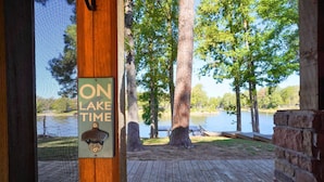 A wooden deck with a sign reading "ON LAKE TIME" and a view of a lake surrounded by trees.