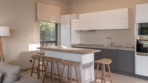 Een moderne keuken met een centraal eiland, barkrukken en een groot raam.