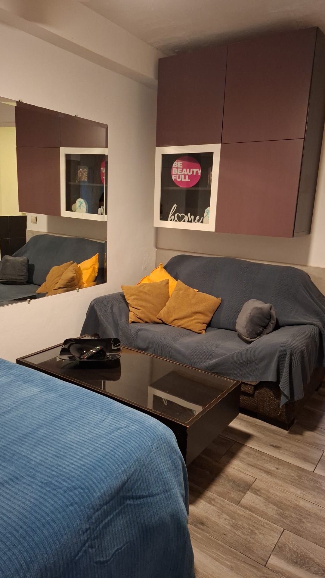 A modern bedroom with a grey sofa, a small table, and a mirror.