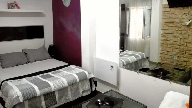 Un dormitorio con cama, una mesita de noche, un espejo, un reloj y un televisor montado en la pared.