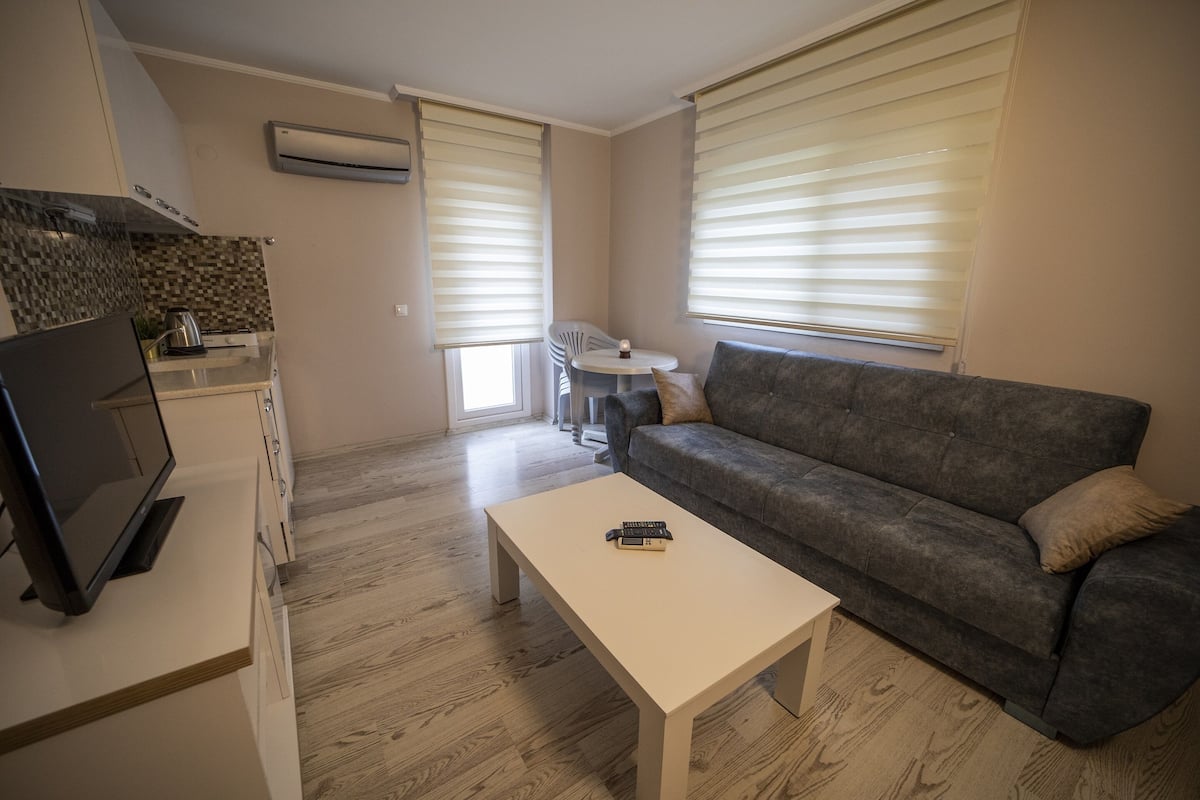 A modern living room with a grey sofa, a white coffee table, and a TV on a stand.