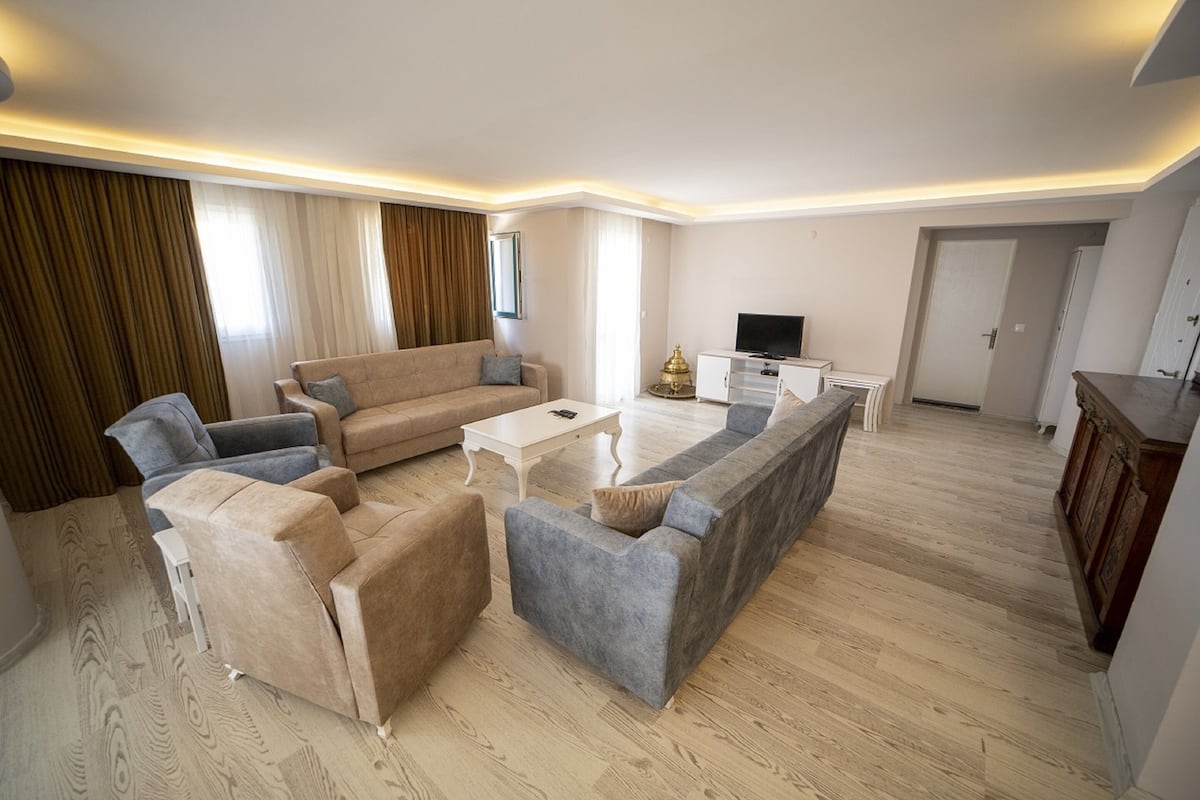 A modern living room with a beige sofa, a grey sofa, a white coffee table, and a TV on a white cabinet.