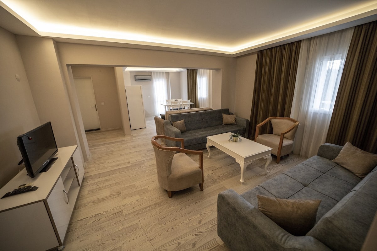 A modern living room with a grey sofa, two armchairs, a coffee table, and a TV on a cabinet.