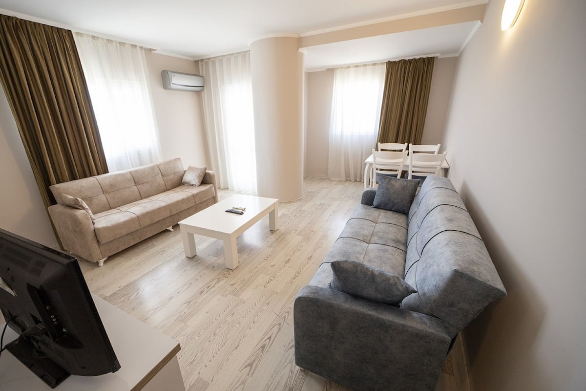 A modern living room with a beige sofa, a grey sofa, a white coffee table, and a TV on a stand.