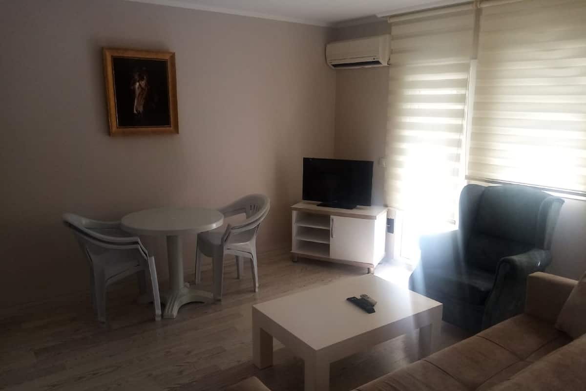 A living room with a sofa, a television on a stand, a small table, and two chairs.