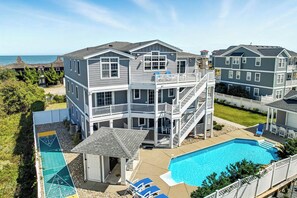 A multi-story residential building with a pool, a tennis court, and a covered patio area.