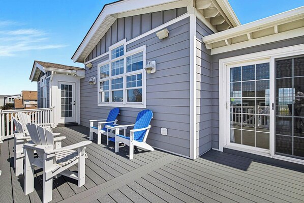 A deck with two Adirondack chairs and a small table, a sliding glass door, and a window with a view of the deck.