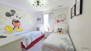 A child's bedroom with Mickey Mouse decorations, two beds, a desk, and a ceiling fan.