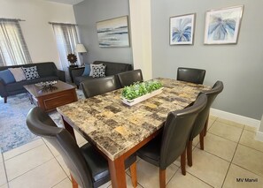 A dining area with a marble table, black chairs, and a centerpiece of green plants.