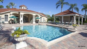 A pool area with lounge chairs, a covered seating area, and a building with a tiled roof. - Asteria – Your perfect stay close to Theme Parks. (Kissimmee)