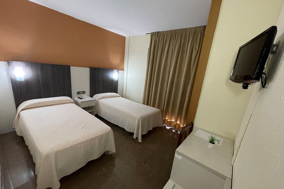 Habitación de hotel con dos camas, un televisor, un escritorio y una ventana con cortinas.
