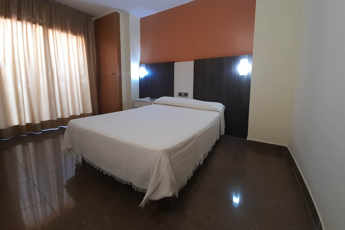 Una habitación de hotel con una cama grande, una mesita de noche, un armario de madera y un espejo con iluminación.