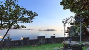 A waterfront view with a stone wall, a metal gate, and a grassy area. - Maison du Lac (Piemonte)