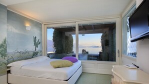 A bedroom with a bed, a TV, and a view of a body of water. - Maison du Lac (Piemonte)