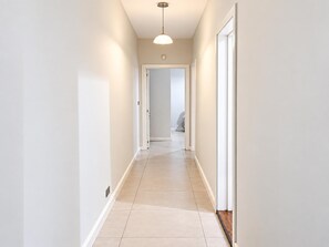 Un couloir étroit, aux couleurs claires, avec un luminaire au plafond et une porte au bout.