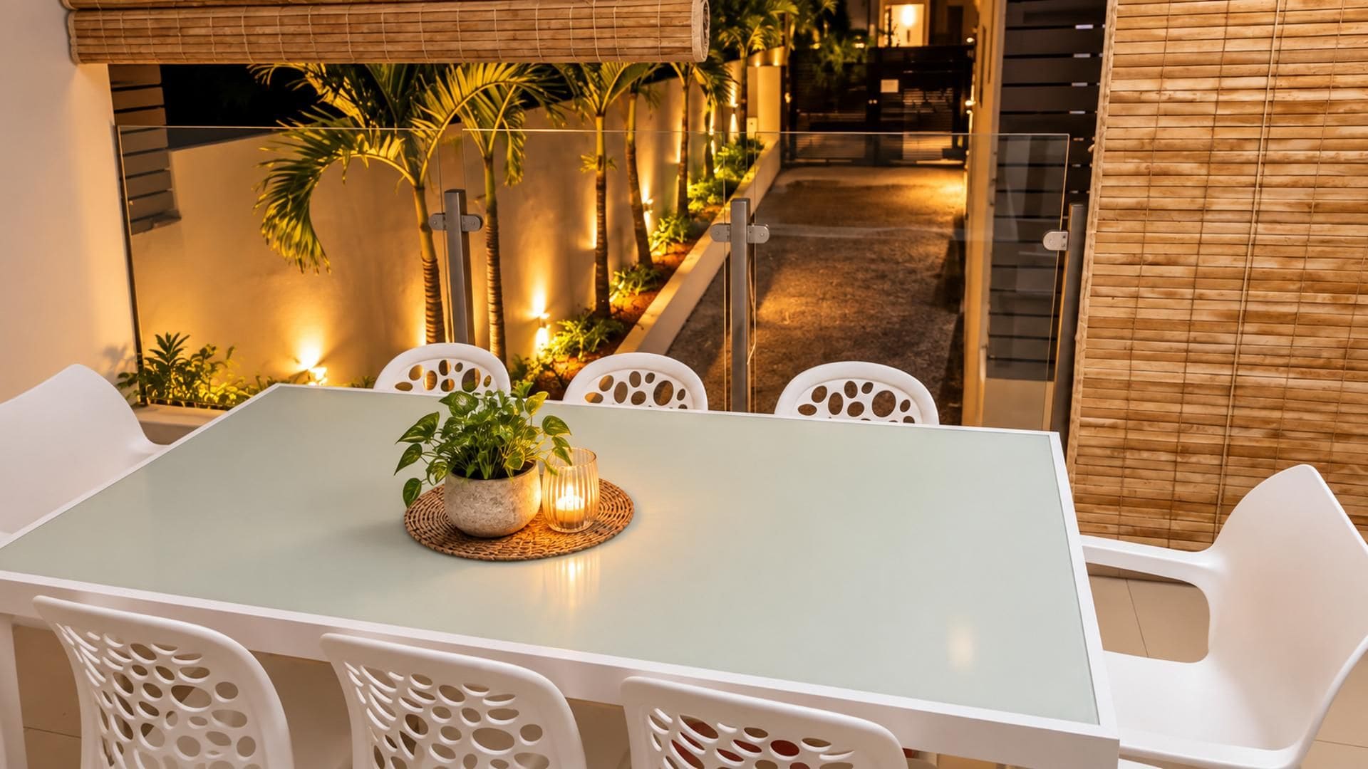 A dining area with a table and chairs, a potted plant, and a view of a garden with palm trees.