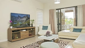 A living room with a flat-screen TV, wooden entertainment unit, beige sofa, and a glass coffee table. - Modern 2-bed Sleeps 4 With Balcony (Grand-Baie)