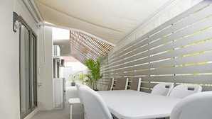 A covered outdoor dining area with a table and chairs, a potted plant, and a view of the street. - Modern 2-bed Sleeps 4 With Balcony (Grand-Baie)