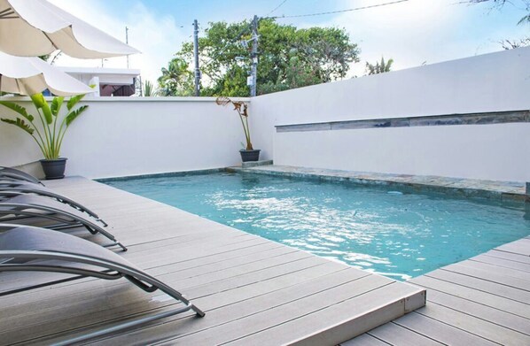 A swimming pool with a wooden deck, surrounded by white walls and potted plants. - Modern 2-bed Sleeps 4 With Balcony (Grand-Baie)