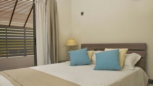 A hotel room with a bed, a lamp, and a window with blinds. - Modern 2-bed Sleeps 4 With Balcony (Grand-Baie)