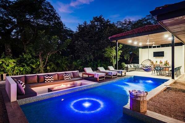 A swimming pool with a fire feature, lounge chairs, and a covered seating area with a table and chairs. - Luxury Retreat: Private Pool, Fire Pit + Exclusive Beach Club – 4 Min to the Beach (Tamarindo)