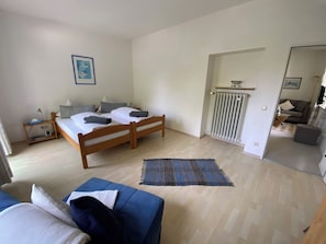 Un dormitorio con una cama de madera, una mesita de noche, un sofá azul y vista al área de estar.